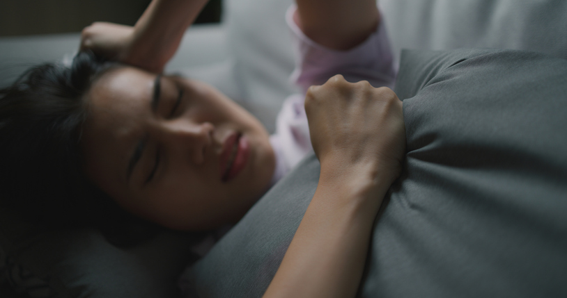 Femme allongée dans le noir, agrippant son oreiller sans parvenir à dormir
