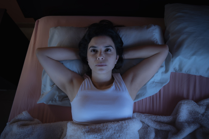 Femme éveillée dans son lit la nuit, bras derrière la tête, yeux ouverts